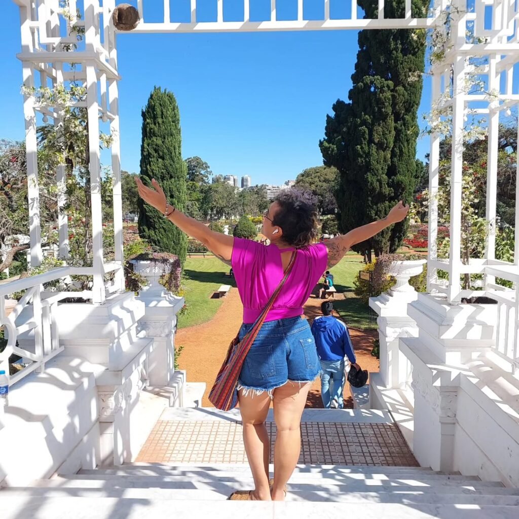 emocionanda de shorts jeans e blusinha roxa de costas, de braçoas abertos, no Parque O Rosendal