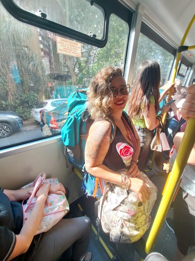 Eu com minha em pé no ônibus com a minha mochilona e um mochila a mais segurando uma rosa na mão.